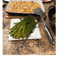 Eggs Benedict casserole in a white baking dish, and roasted asparagus on a white platter